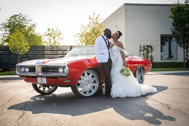 Newlyweds kissing beside a classic red Pontiac by Ken Floyd Media